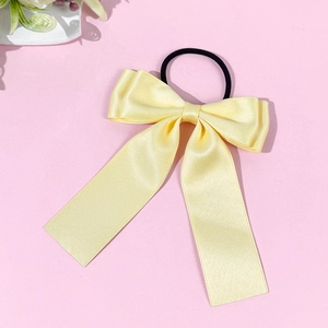 Détail d'un chouchou à nœud en satin jaune clair avec rubans sur fond rose