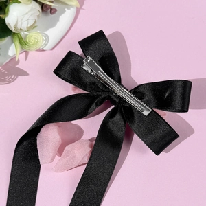 Elegante fermaglio per capelli con fiocco in raso nero e lunghi nastri su sfondo rosa