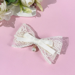 Détail d'une barrette en dentelle blanche avec pendentif perle et nœud en ruban satiné