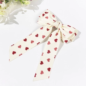 Detail of cream bow hair clip with red heart pattern and long satin streamers