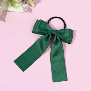 Détail d'un chouchou élégant en satin vert foncé avec ruban sur fond rose doux