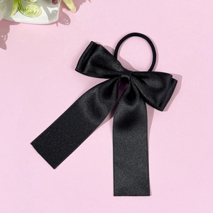 Gros plan d'un chouchou en satin noir avec de longs rubans sur fond rose tendre
