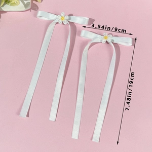 Detail of white satin bow hair clips with daisy flower centers and long ribbons