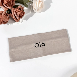 Close-up of oatmeal knitted yoga headband with black Ola text and floral accent