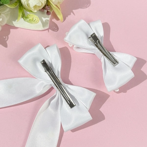 Détail de barrettes nœuds en satin blanc avec pinces crocodiles en métal sur fond rose