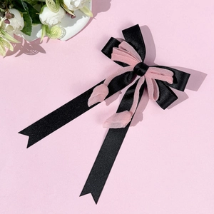 Dettaglio di un fermaglio per capelli con nastri di raso neri e fiori di organza rosa