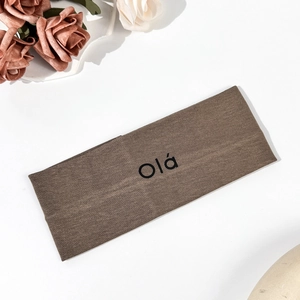 Detail of a brown ribbed knit sports headband featuring black Olá printed text
