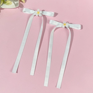 Detail of white satin ribbon bow hair clips featuring embroidered daisy flower accents