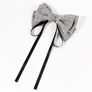 Detail of floral bow hair clip with lace trim and black satin ribbons on white backdrop
