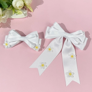 Gros plan de barrettes à nœud en satin blanc avec motifs de marguerites brodés fins