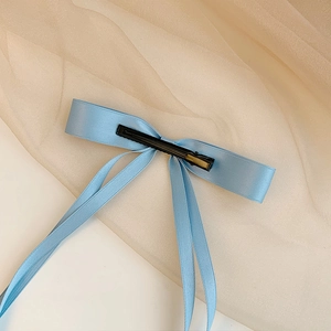 Close-up of a light blue satin ribbon bow hair clip with a silky glossy texture
