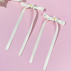 Detail showing white ribbon bow hair clips with daisy floral center and woven texture