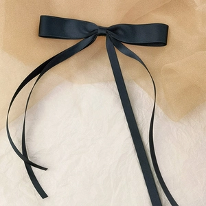 Detail of elegant black ribbon bow hair clip with long streamers on refined backdrop