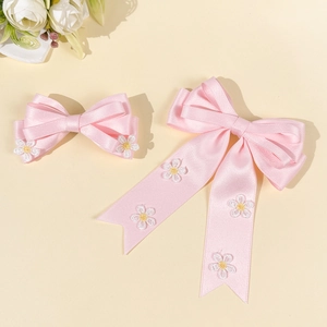 Détail de nœuds à cheveux en satin rose avec marguerites brodées et longs rubans
