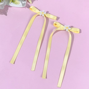 Detailed close-up of yellow satin ribbon hair clips with white daisy flower embroidery