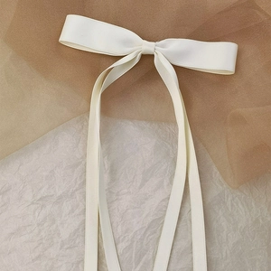 Close-up of cream-white ribbon bow hair clip with elegant long streamers and ribbed texture