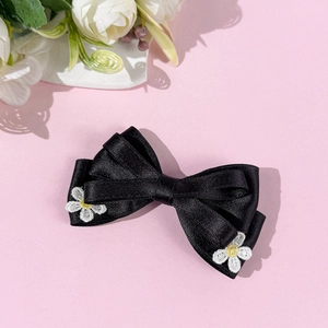 Détail de la barrette à nœud en satin noir avec broderie de marguerites sur fond rose