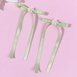 Set of two light green satin bow hair clips with daisy embroidery on pink background