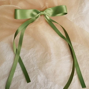 Detailed close-up of grass green satin ribbon bow hair clip with elegant long streamers