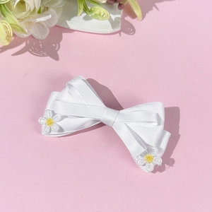 Détail d'un nœud à cheveux en satin blanc avec fleurs de marguerite brodées et texture soyeuse