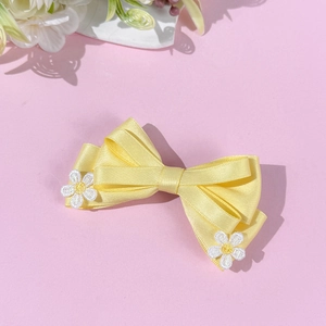 Détail d'une pince à cheveux nœud en satin jaune avec fleurs de marguerite sur fond rose