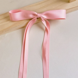 Macro shot of pink satin bow hair clip with long ribbons on a textured wooden background