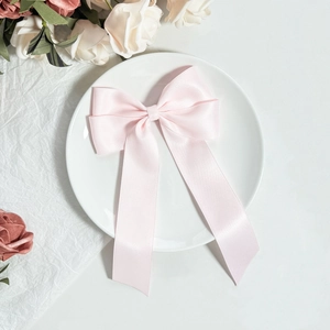Détail d'une pince à cheveux nœud en satin rose clair avec de longs rubans sur céramique