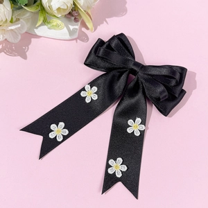 Détail d'un nœud papillon en satin noir avec broderie de marguerites sur fond rose