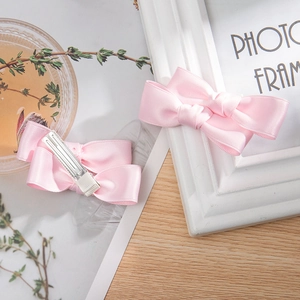 Pair of pink satin double bow hair clips with silver metal crocodile grip on a warm desk