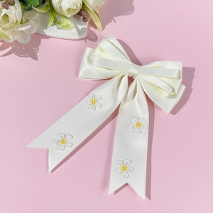 Détail d'un nœud à cheveux en satin crème orné de marguerites brodées blanches