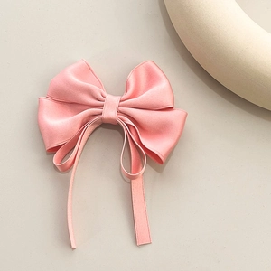 Elegant pink satin bow hair clip with long ribbons on a minimalist beige background
