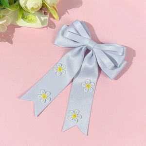 Détail de la pince à cheveux noeud en satin bleu clair avec broderie marguerite et rubans