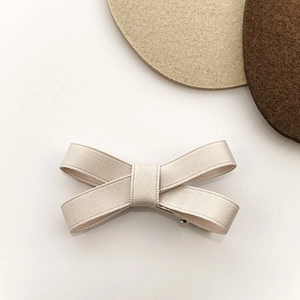 Minimalist cream ribbon bow hair clip with ribbed texture on clean aesthetic background