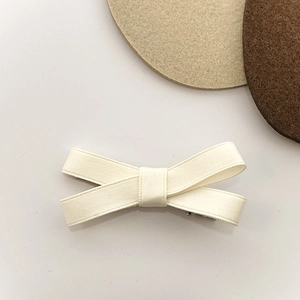 Detailed close-up of cream-white ribbon bow hair clip with textured fabric and metal clip