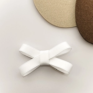 Close-up of white ribbon bow hair clip with textured fabric and metal alligator grip