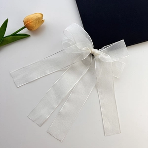 Close-up of white organza ribbon hair clip with long streamers on a grey surface