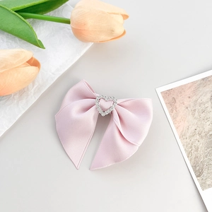 Détail d'une pince à cheveux avec nœud en satin rose et centre en strass en cœur