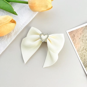 Détail d'un nœud papillon en satin blanc crème avec un cœur scintillant en strass
