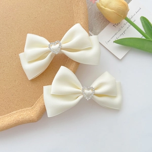 Détail de barrettes à nœuds en satin crème ornées de strass étincelants en forme de cœur