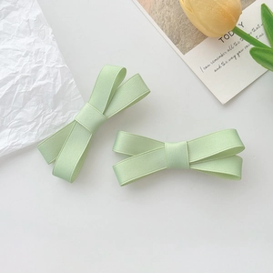 Détail de deux barrettes à cheveux à nœud vert clair en tissu texturé au style épuré