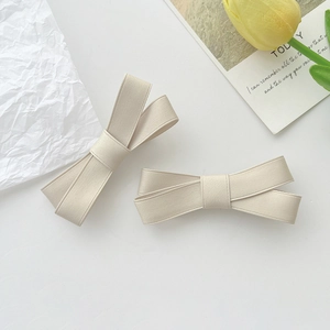 Détail de deux barrettes à nœuds en ruban gros-grain beige sur un fond épuré doux