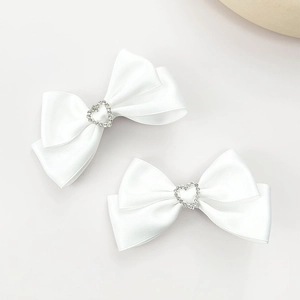 Gros plan sur une paire de barrettes noeuds en satin blanc avec strass en forme de cœur
