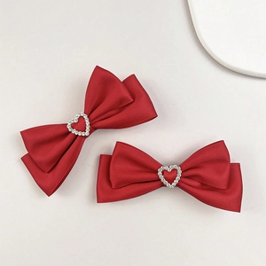 Détail de barrettes à nœuds en satin rouge avec un cœur en cristal étincelant au centre