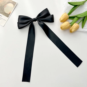 Detail of large black satin bow hair clip with elegant long ribbons on a white surface