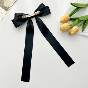 Classic black satin bow hair clip with long streamers on minimalist white background