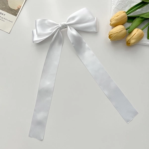 Detail shot of a white satin bow hair clip with long ribbons on a cream background