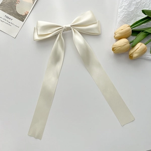 Elegant cream satin bow hair clip with long ribbons on a minimalist white background