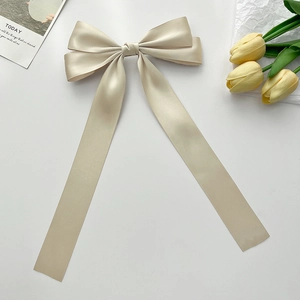 Detailed view of a champagne satin bow hair clip with elegant long flowing ribbons