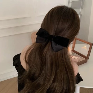 Detail of a large black velvet bow hair clip with ribbons on long brown hair