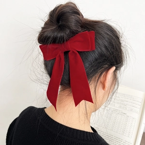 Macro detail of red velvet bow hair clip worn elegantly on a messy bun hairstyle